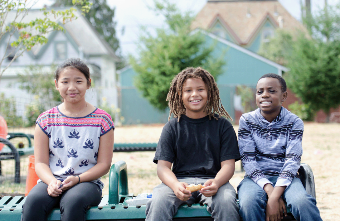 Three students sit on a bench outside a Portland school.